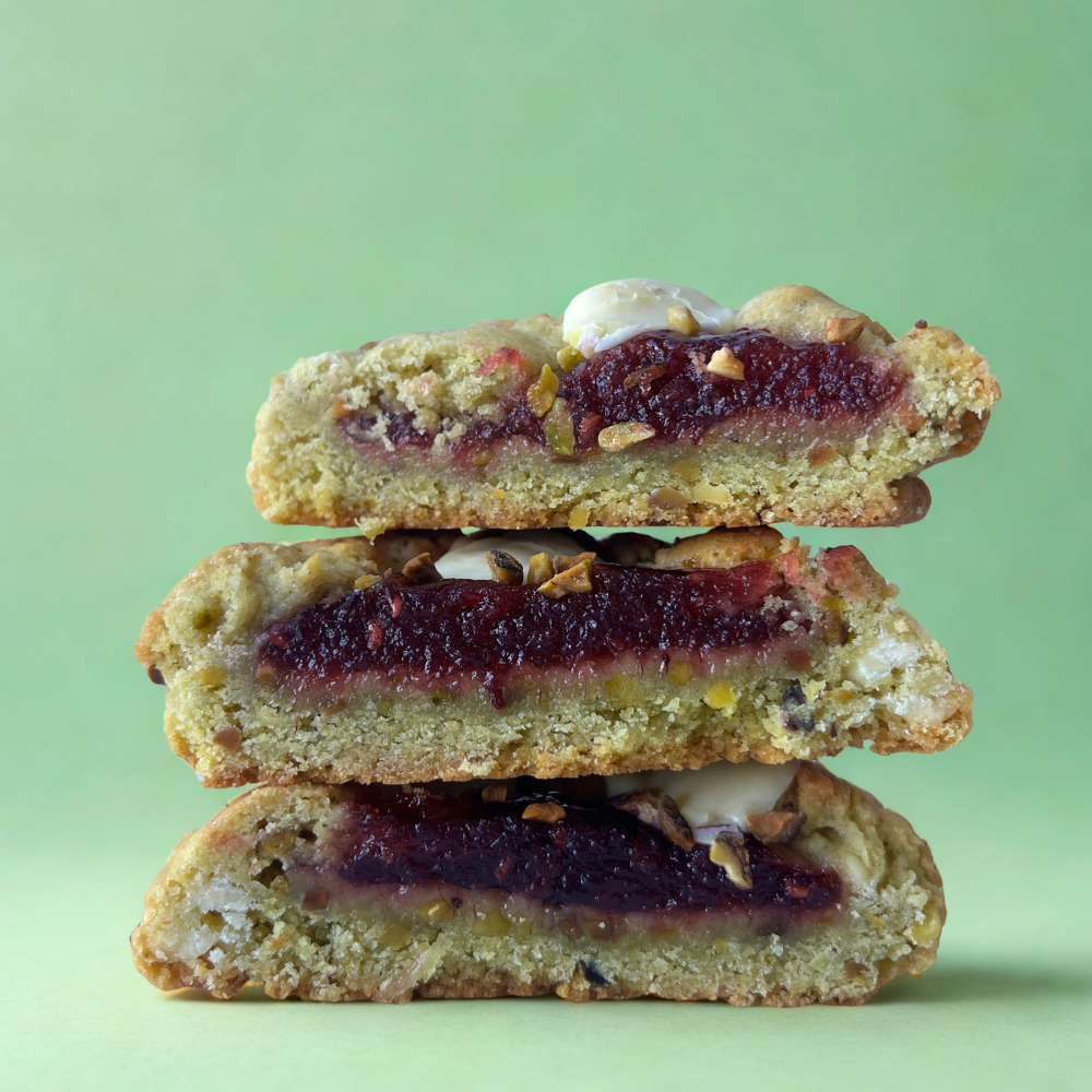 cookies pistaches framboises coupés en deux, avec des brisures de pistaches, un confit framboise en coeur coulant et du chocolat blanc